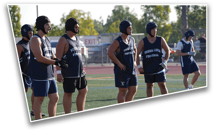 Several people wearing dark sports uniforms and protective headgear stand on a field, appearing to prepare for or participate in a football activity. Description generated by AI