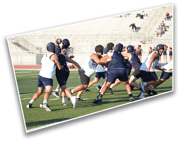 Adults wearing helmets and athletic clothing are playing a contact sport on a grassy field with stadium seating in the background. Description generated by AI