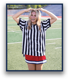 A person with long wavy hair wearing a black and white striped shirt and a red skirt stands on a sports field with arms raised above their head. Description generated by AI