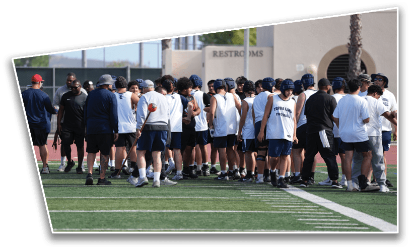A group of people wearing athletic clothing and helmets are gathered on a sports field near a building with a sign that says restrooms. Description generated by AI