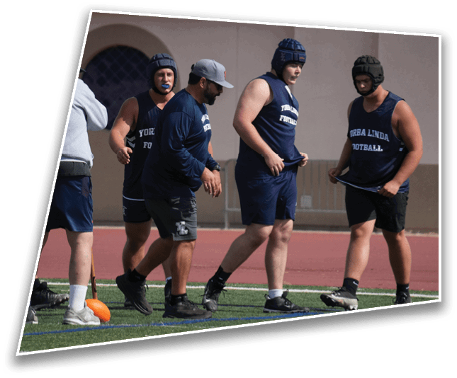 People wearing sports helmets and athletic clothing stand on a field, appearing to prepare for or participate in a football practice or training session. Description generated by AI