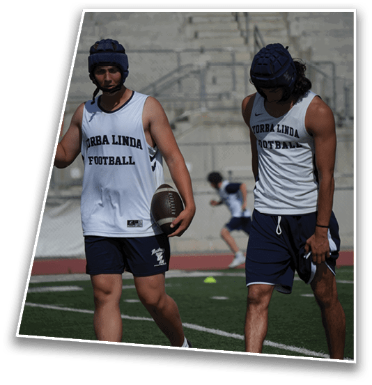 Two people wearing protective headgear and sleeveless sports jerseys stand in front of empty stadium bleachers. Description generated by AI