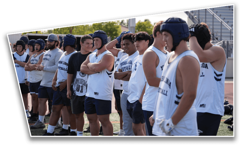 A group of people wearing sports helmets and athletic clothing stand in a line outdoors, some with arms crossed and others with hands on hips. Description generated by AI