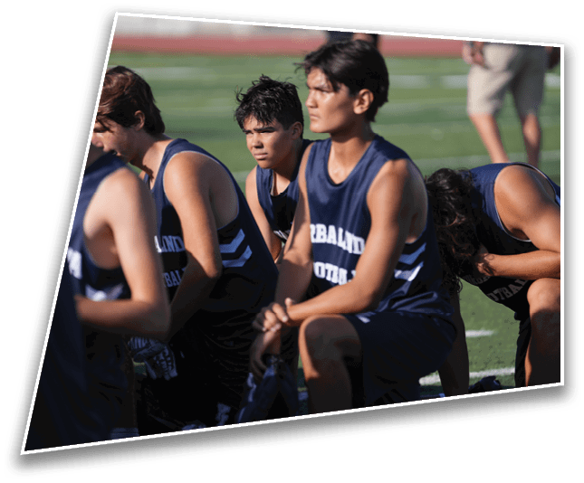 A group of people wearing dark blue sports uniforms are kneeling on a grassy field, appearing focused and attentive. Description generated by AI