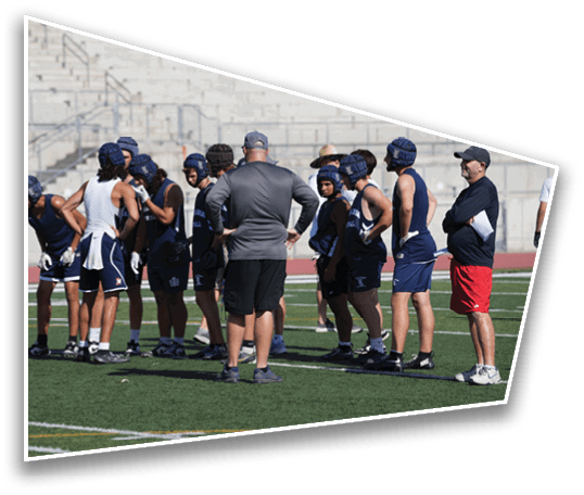 A group of people wearing athletic gear and helmets stand on a sports field while one person in a gray shirt and black shorts appears to be coaching or instructing them. Description generated by AI