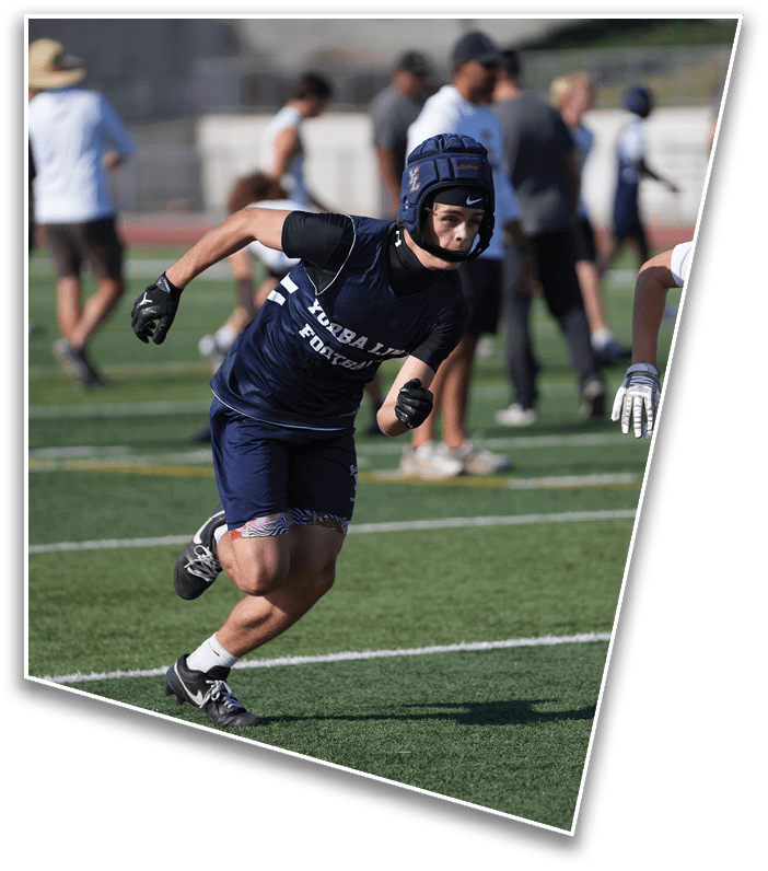 A person wearing a protective helmet and sportswear is running on a football field while another person with gloves reaches out toward them. Description generated by AI