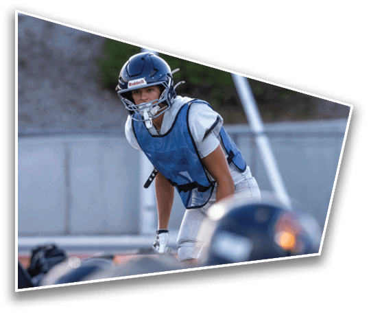 A person wearing a football helmet and blue practice vest is leaning forward on a field with other players in the foreground. Description generated by AI
