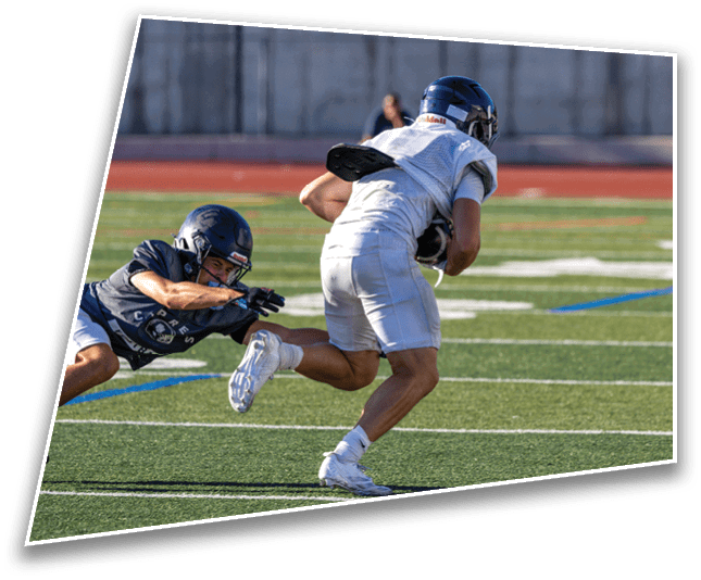 Two people in football gear are on a field with one person running while holding the ball and the other person diving to tackle them. Description generated by AI