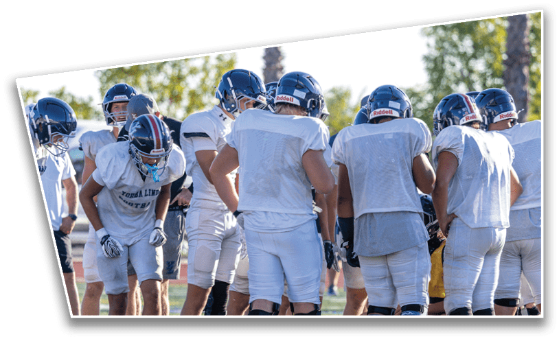 A group of people wearing white football uniforms and helmets are gathered closely together outdoors on a sunny day. Description generated by AI