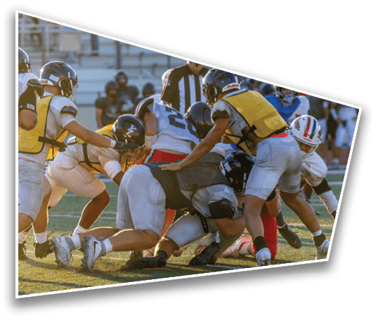 Several people wearing football helmets and uniforms are engaged in a close physical play on a grassy field during a game. Description generated by AI