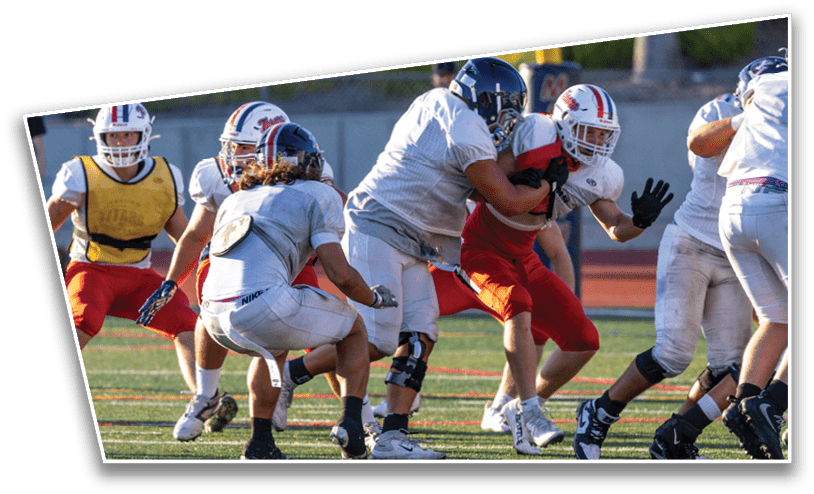 Several people wearing football helmets and uniforms are engaged in a play on a football field with one person in red being tackled by others in white and gray. Description generated by AI