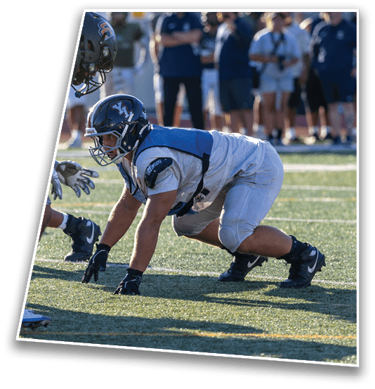 People in football gear are crouched on a field in a ready stance, preparing for a play. Description generated by AI