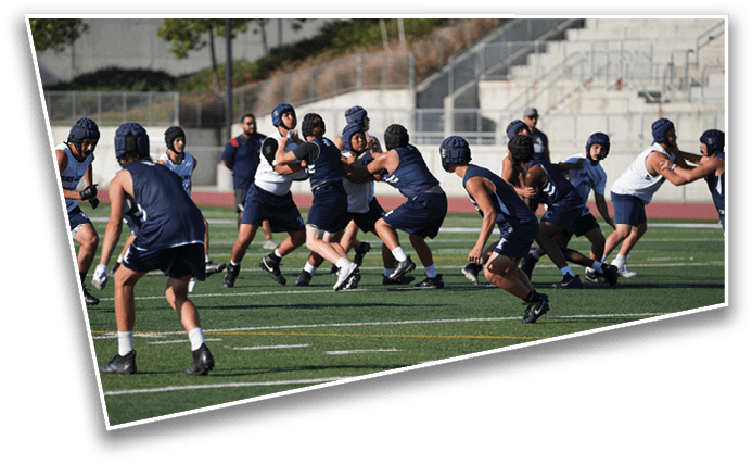 People wearing helmets and athletic clothing are playing a contact sport on a grassy field with a stadium in the background. Description generated by AI
