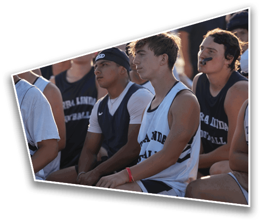 Several people wearing sports jerseys are sitting closely together, appearing attentive and engaged, with one person wearing a mouthguard. Description generated by AI