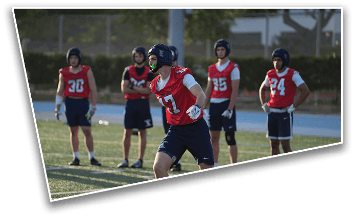 A group of people wearing red sports jerseys and helmets are standing and running on a grassy field during a sports practice or game. Description generated by AI