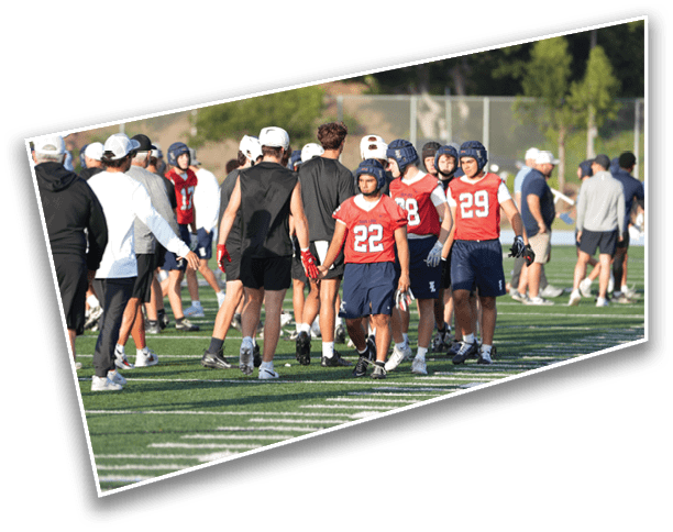 People wearing sports uniforms and helmets are walking on a football field while others in casual clothing stand nearby. Description generated by AI