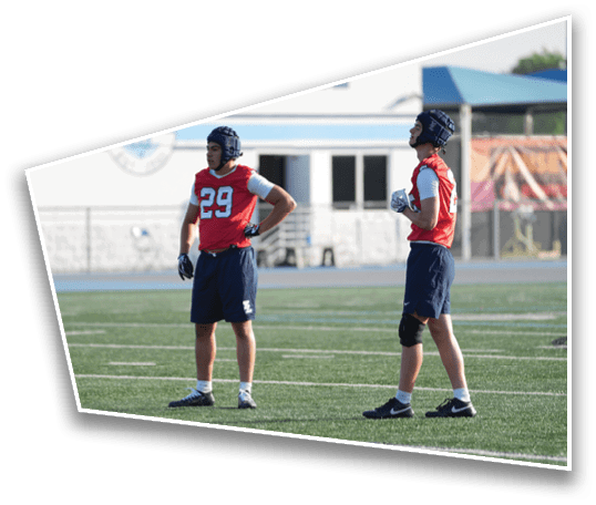 Two people wearing red sports jerseys and helmets stand on a football field during practice or a game. Description generated by AI