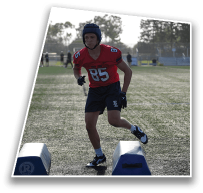 A person wearing a red sports jersey and helmet is running between two blue training pads on a grassy field during daylight. Description generated by AI