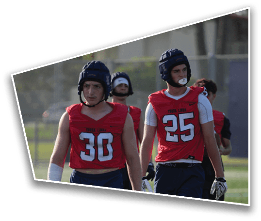 Four people wearing red sports jerseys and protective helmets are standing outdoors, with two of them in the foreground and two in the background. Description generated by AI