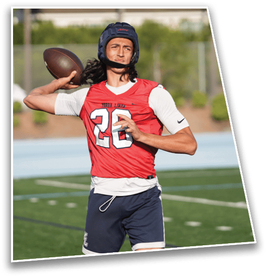 A person wearing a red sports jersey and protective headgear is preparing to throw a football on a grassy field. Description generated by AI