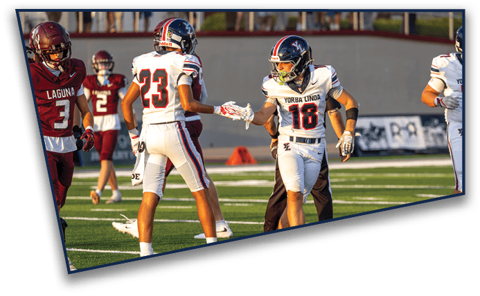 Two people in football uniforms are giving each other a handshake or high-five on a football field during a game. Description generated by AI