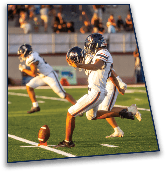 Two people wearing football helmets and uniforms are facing each other on a field with blurred spectators in the background. Description generated by AI