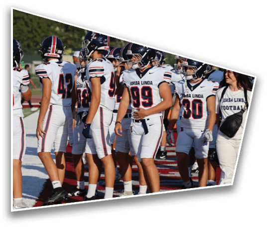 A group of people wearing white football uniforms with helmets are standing together on a field during daylight. Description generated by AI