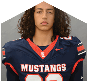 Person with long curly hair wearing a navy blue and red Mustangs football jersey looking directly at the camera against a plain gray background. Description generated by AI