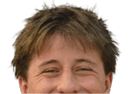 A person with short hair is smiling and wearing a navy blue football jersey with red and white accents that says Mustangs and has the number 77. Description generated by AI