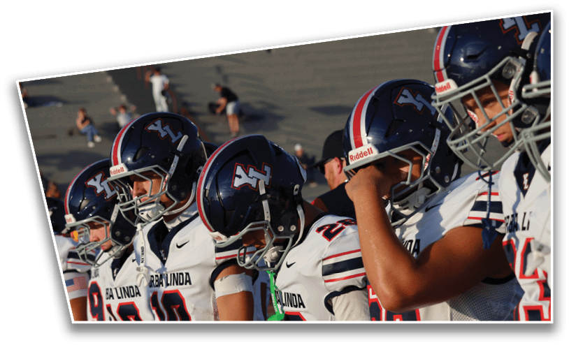 A group of people wearing football helmets and white jerseys with “LA LINDA" written on them are standing closely together on a field. Description generated by AI