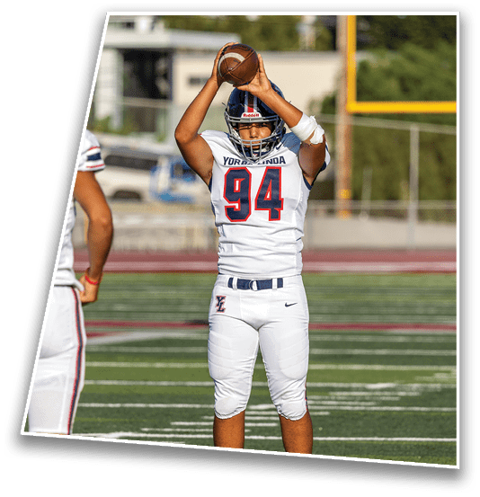 A person wearing a football helmet and jersey with the number 94 is holding a football above their head, preparing to throw it. Description generated by AI