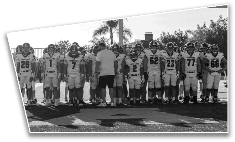 A group of people in football uniforms stands in a line on a field with one person in casual clothing standing among them. Description generated by AI