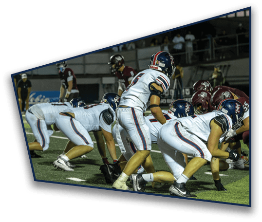 People in football uniforms are lined up on a field facing each other, preparing for a play during a game at night. Description generated by AI
