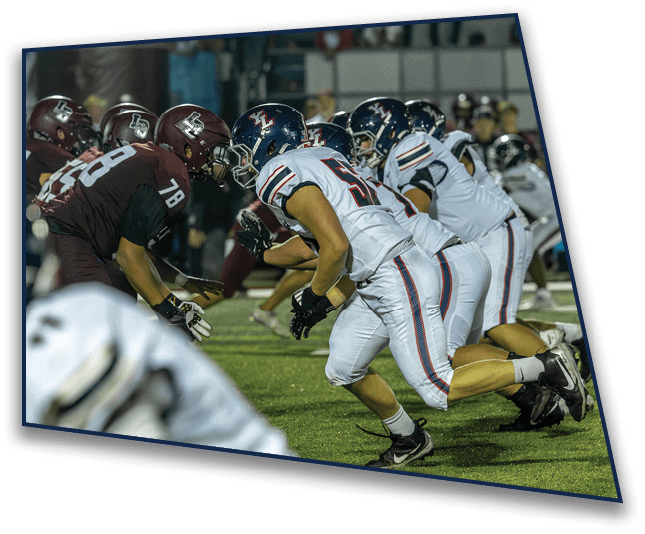 Adults in football uniforms are lined up on a field facing each other in a ready stance during a game. Description generated by AI