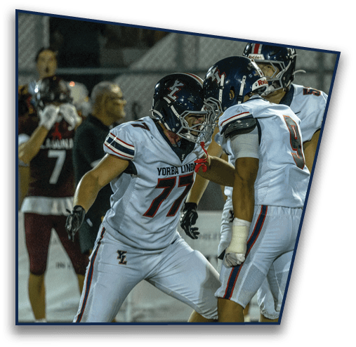 Two people wearing football helmets and Yorba Linda jerseys are facing each other closely in an intense moment on the field. Description generated by AI