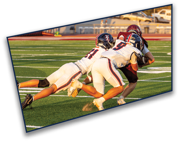 Two people in football uniforms are tackling a third person holding a football on a grassy field with yard lines. Description generated by AI