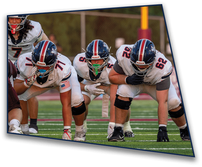 Three people in football uniforms and helmets are crouched in a ready position on a football field. Description generated by AI