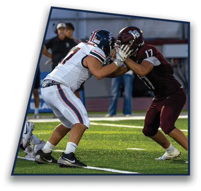 Two people wearing sports uniforms are engaged in a football play on a grassy field near a yard marker. Description generated by AI