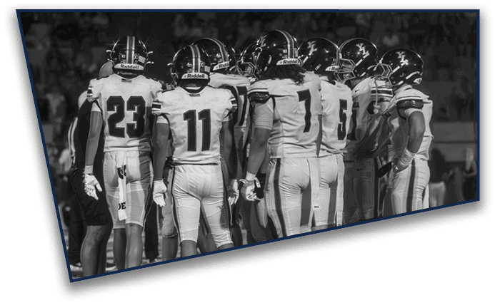 A group of people wearing sports uniforms are standing closely together on a field, seemingly in a huddle or discussion. Description generated by AI