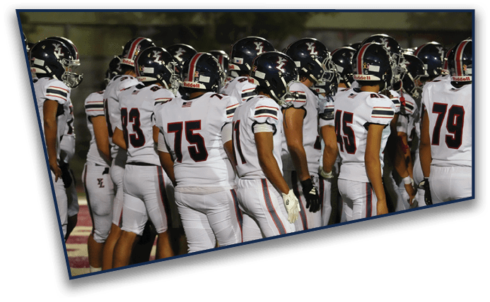 A group of people wearing football helmets and uniforms are standing closely together on a field at night. Description generated by AI
