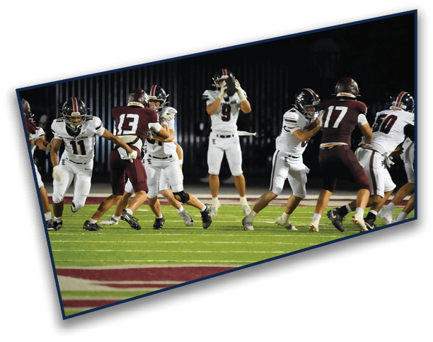 People wearing football uniforms are actively playing on a field under stadium lights during a nighttime game. Description generated by AI
