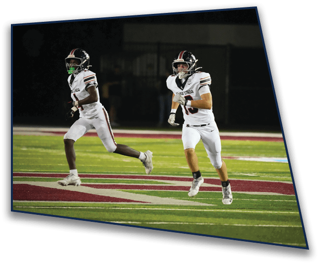 Two people in white football uniforms are running on a field during a nighttime game. Description generated by AI