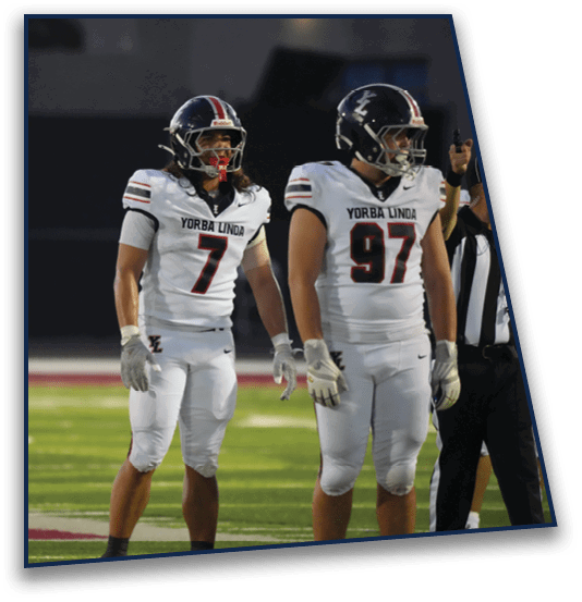 Two people wearing white football uniforms with “Yorba Linda" on the jerseys stand on a football field. Description generated by AI