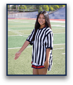 A person with long hair wearing a black and white striped shirt stands on a sports field with one arm extended to the side. Description generated by AI