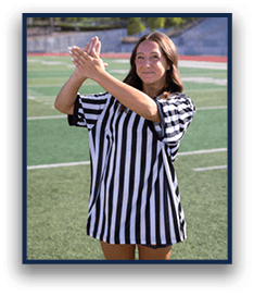 A person wearing a black and white striped referee shirt is standing on a sports field with hands raised and clasped together. Description generated by AI