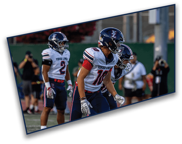 Three people wearing football uniforms and helmets stand on a field with a blurred background of trees and spectators. Description generated by AI