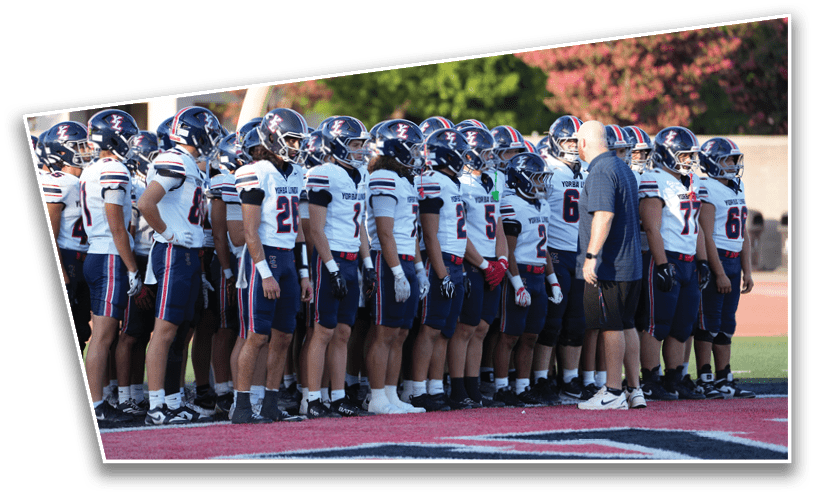 A group of people wearing football uniforms and helmets stand in a line on a field while a person in a blue shirt and shorts speaks to them. Description generated by AI