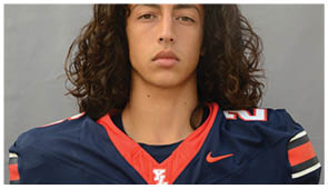 Person with long curly hair wearing a dark blue sports jersey with red and white accents looking directly at the camera. Description generated by AI