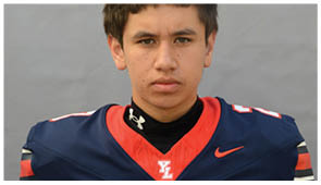 A person wearing a navy blue and red sports jersey with a white “YL" logo and a black Under Armour neck gaiter is looking directly at the camera. Description generated by AI