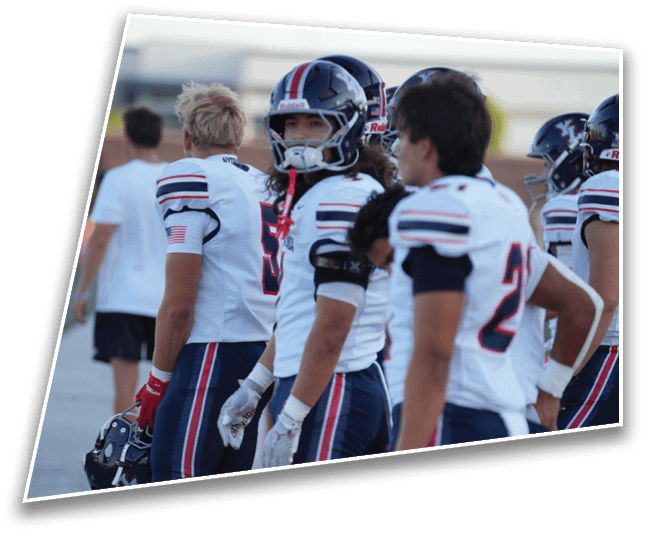 People wearing football helmets and uniforms are standing together, with one person looking directly at the camera. Description generated by AI